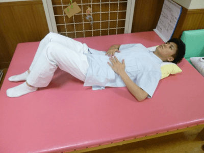 腹式呼吸を行うときの姿勢で横たわるリハビリスタッフ